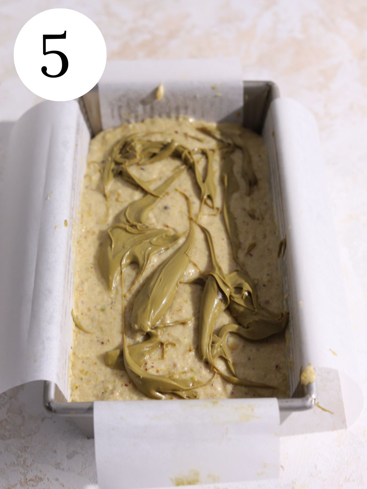 Dollops of green pistachio paste on top of batter in a loaf pan.