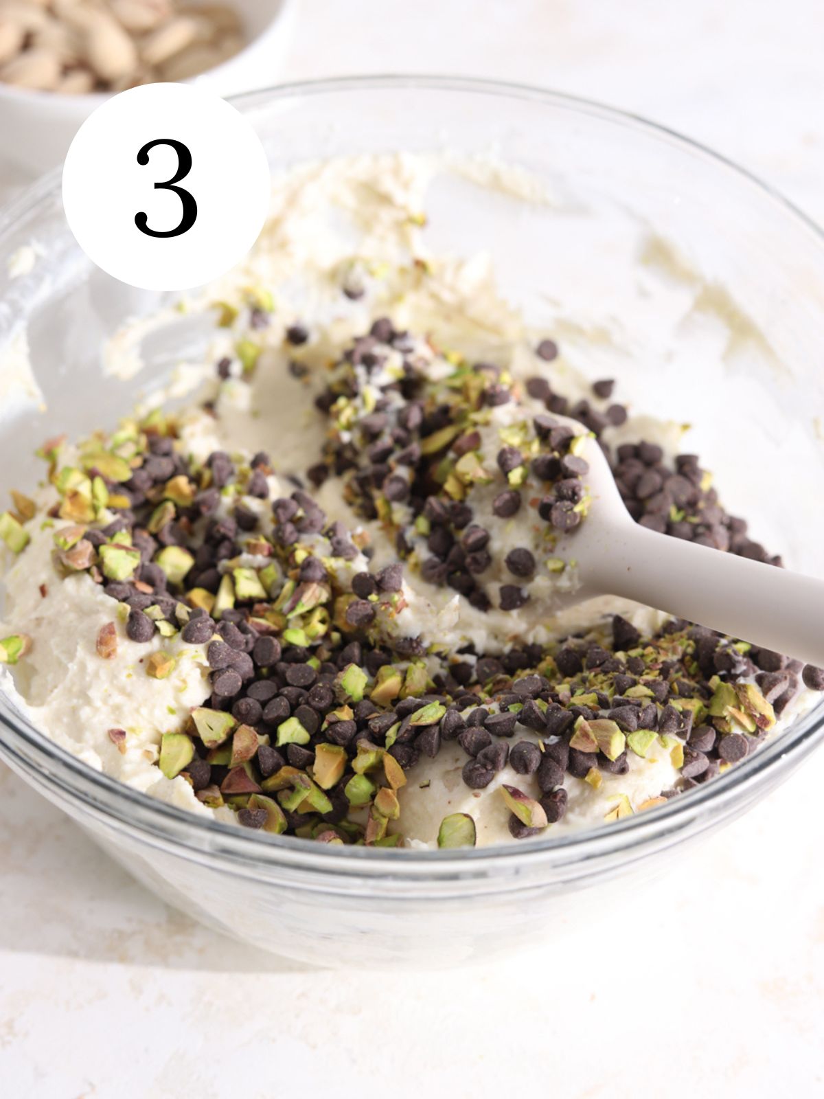 A bowl with pistachios and chocolate chips being stirred into a ricotta cheese mixture. 