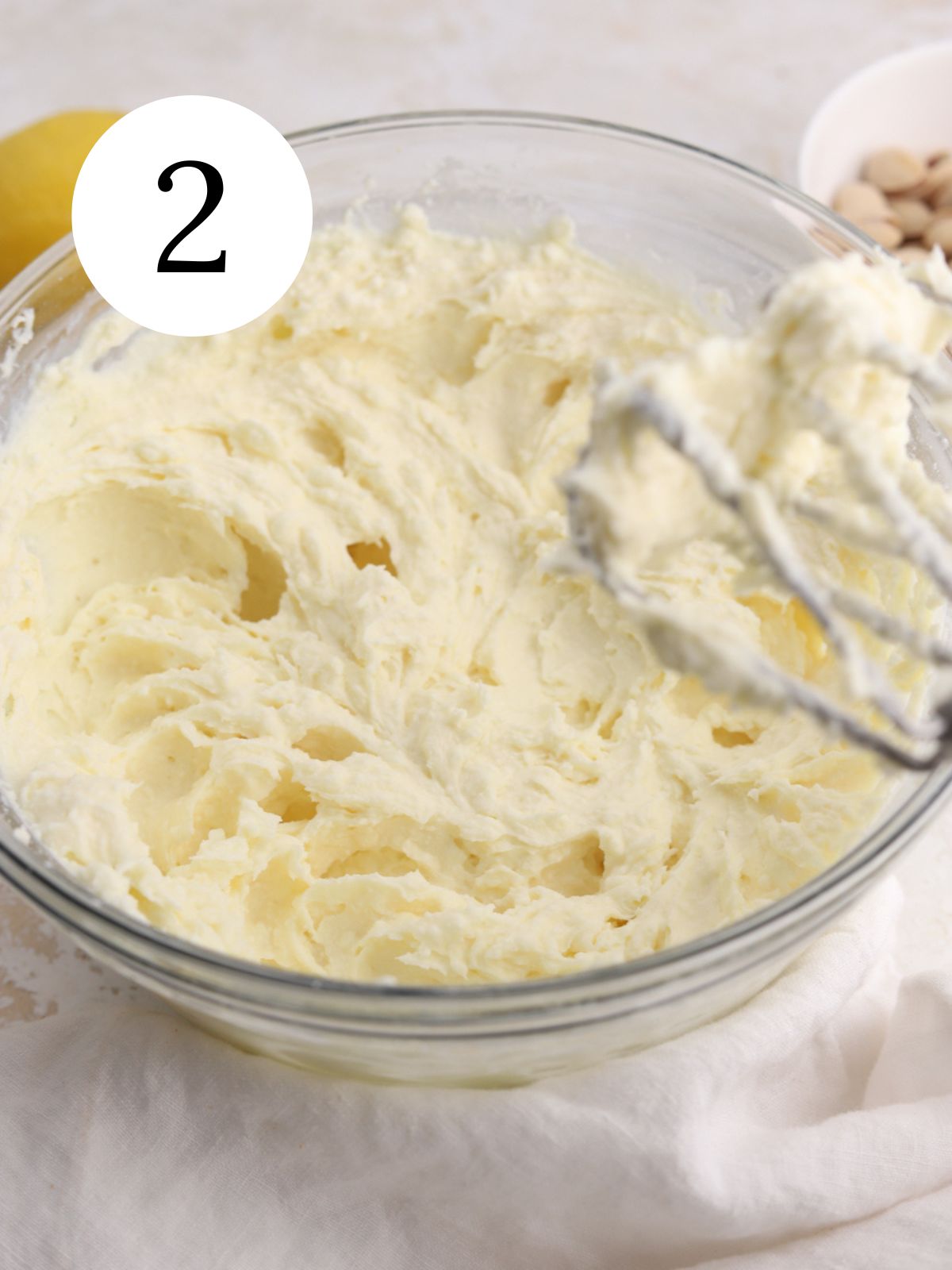 A glass mixing bowl with cream cheese and ricotta mixed with an electric mixer.