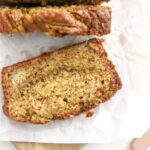 A slice of banana bread with pistachios on parchment paper.