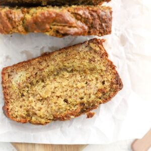 A slice of banana bread with pistachios on parchment paper.