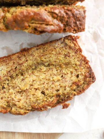 A slice of banana bread with pistachios on parchment paper.
