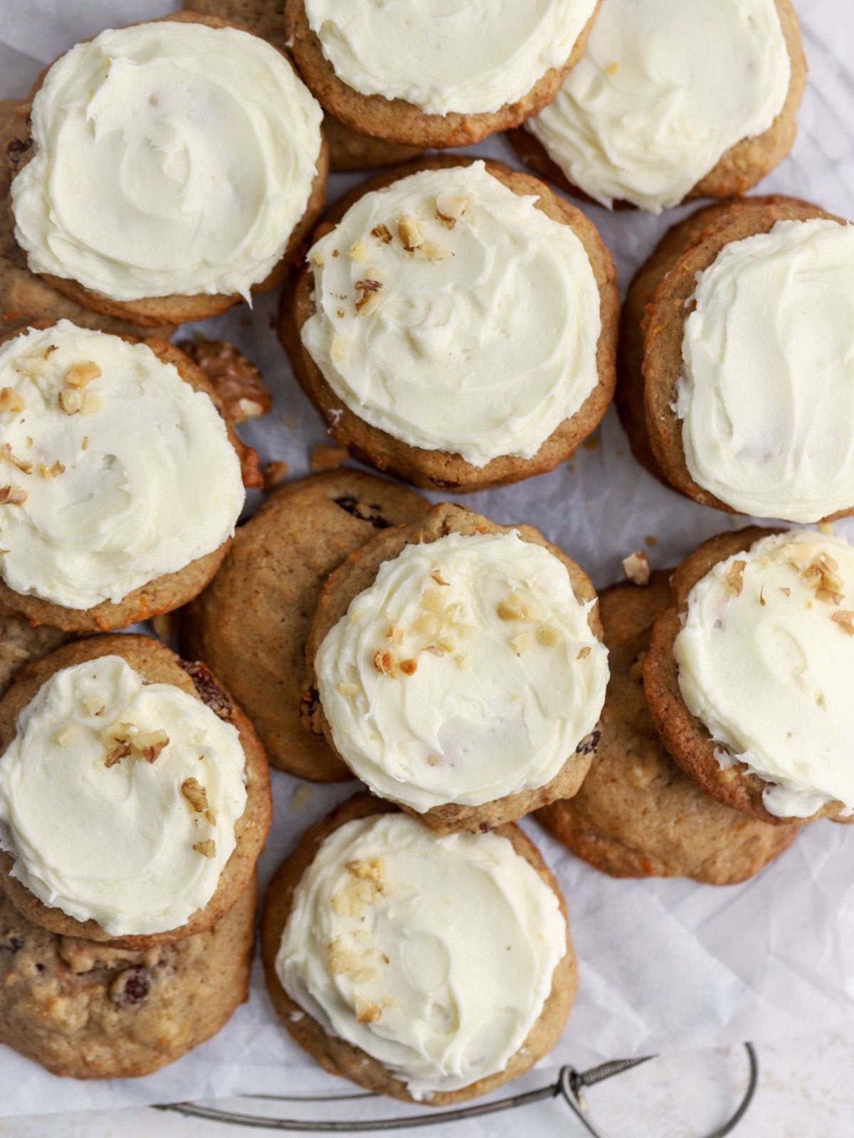A batch of frosted carrot cookies stacked on parchment paper. 