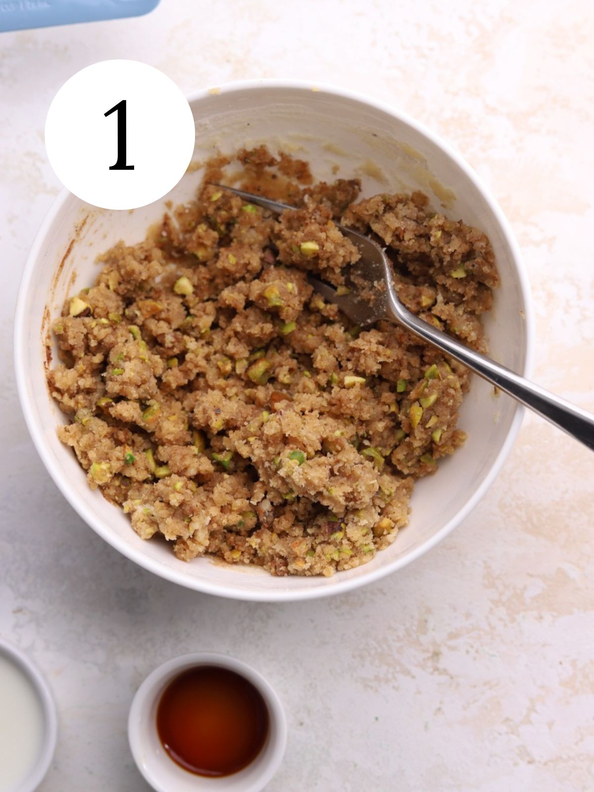 Streusel topping in a bowl with a fork and bowl of vanilla.