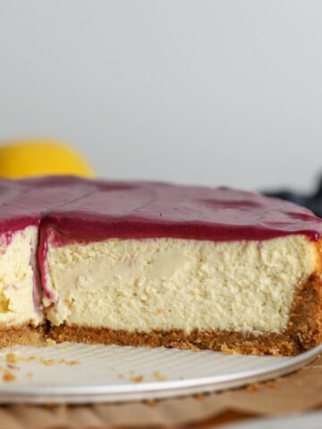 Cheesecake with blueberry curd on top sliced next to some blueberries and a lemon.