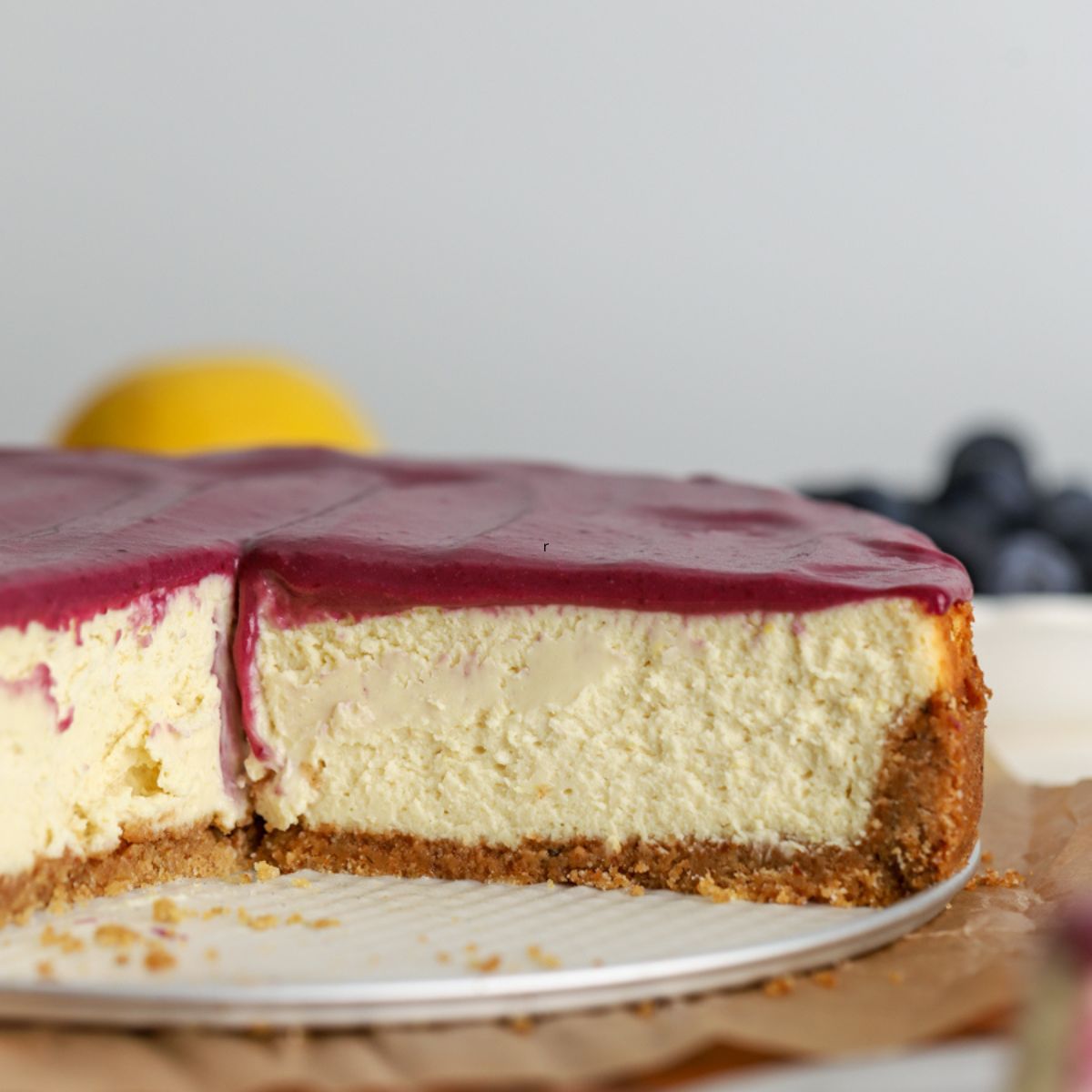 Cheesecake with blueberry curd on top sliced next to some blueberries and a lemon.