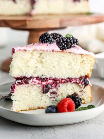 A slice of la two layer cake on a plate with berries on top and next to it.
