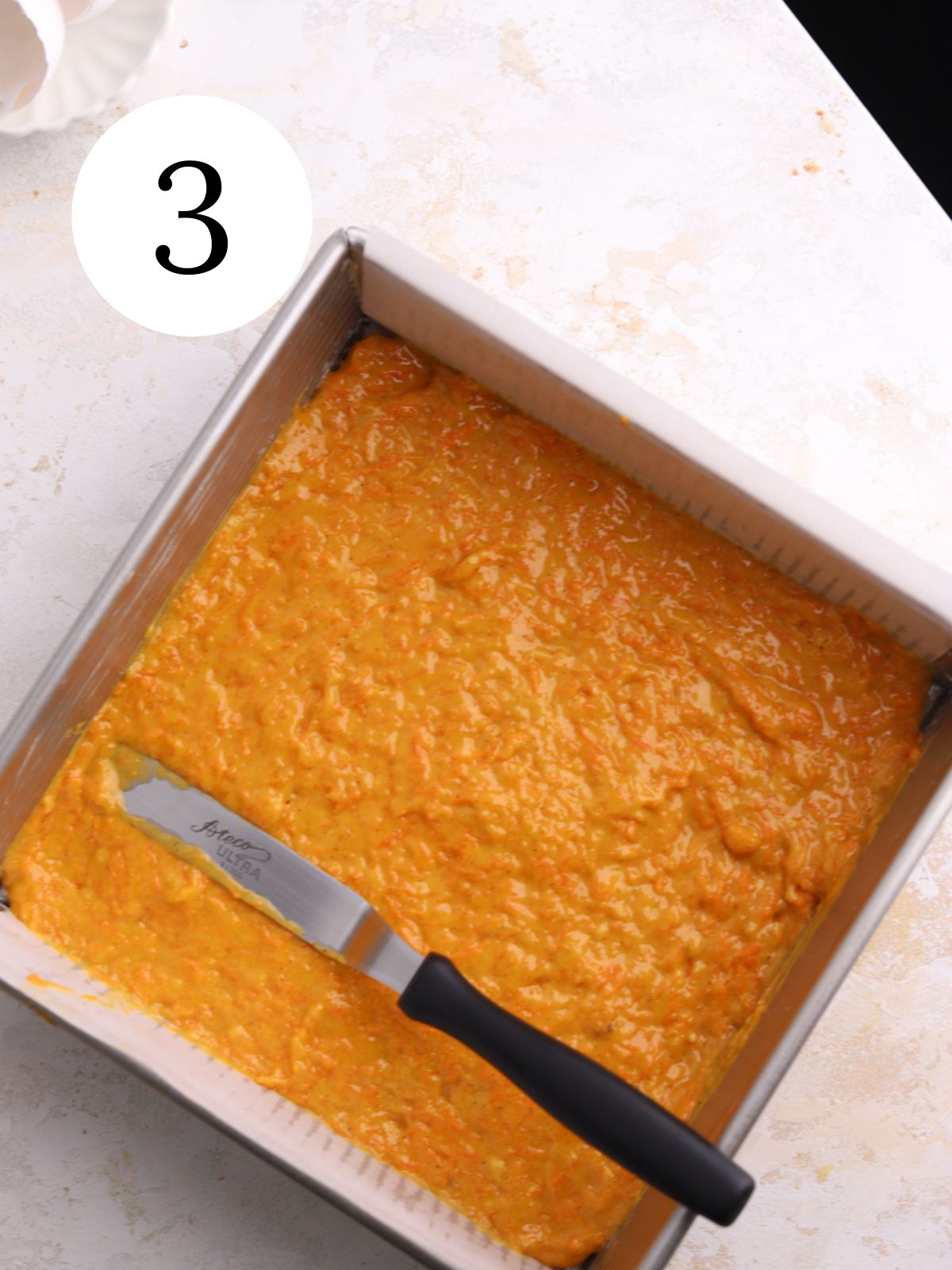 Carrot cake batter in a square pan with an offset spatula.