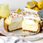 A lemon cheesecake with lemon curd and toasted meringue being sliced.