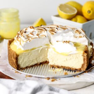 A lemon cheesecake with lemon curd and toasted meringue being sliced.