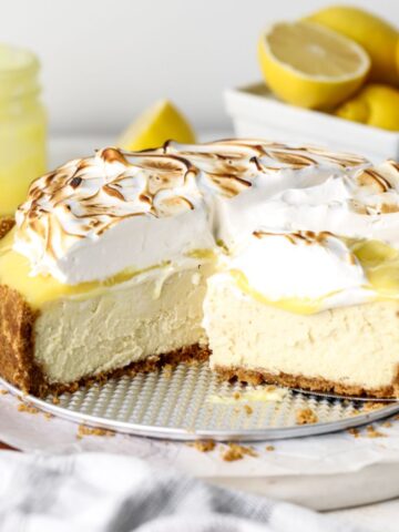 A lemon cheesecake with lemon curd and toasted meringue being sliced.