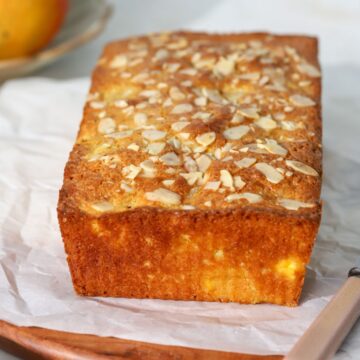 A loaf of mango bread topped with sliced almonds on parchment paper.