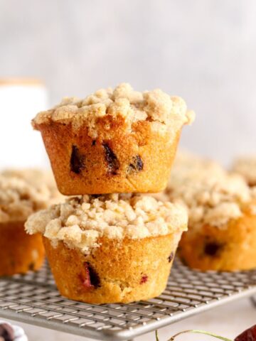 Muffins with streusel topping on a rack next to some cherries.