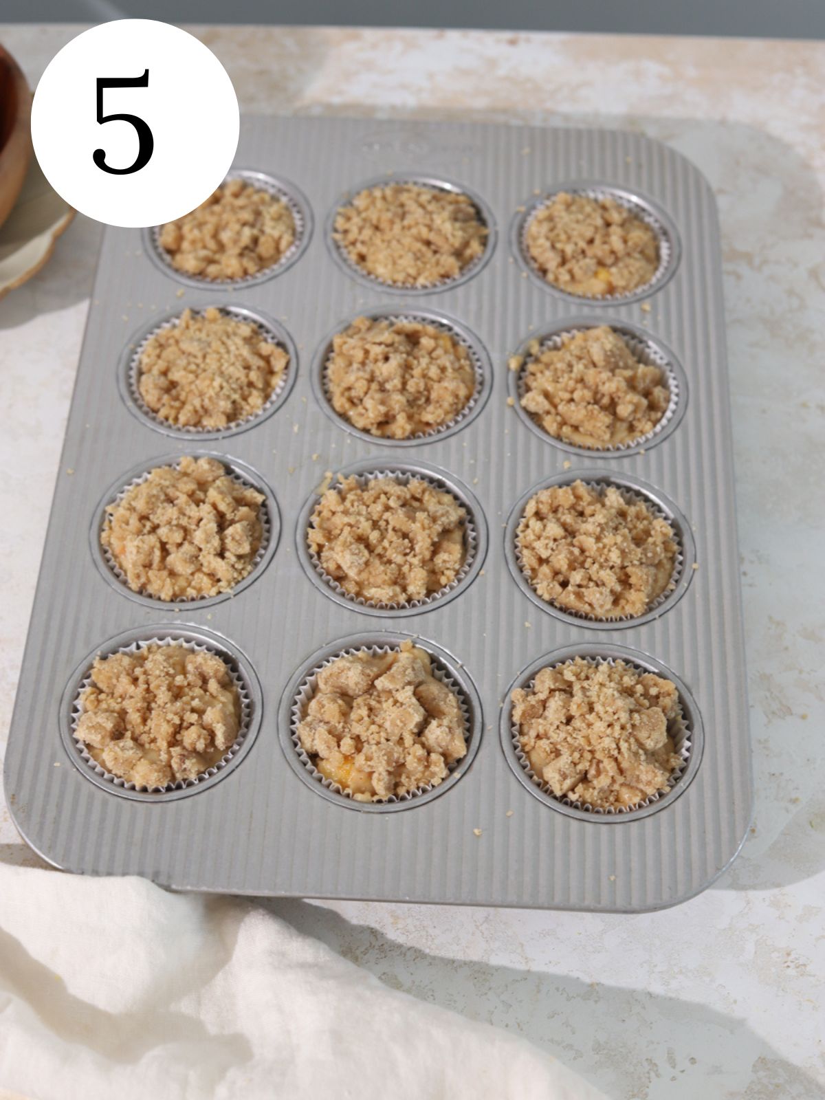 Peach muffin batter with streusel in a muffin pan before baking. 
