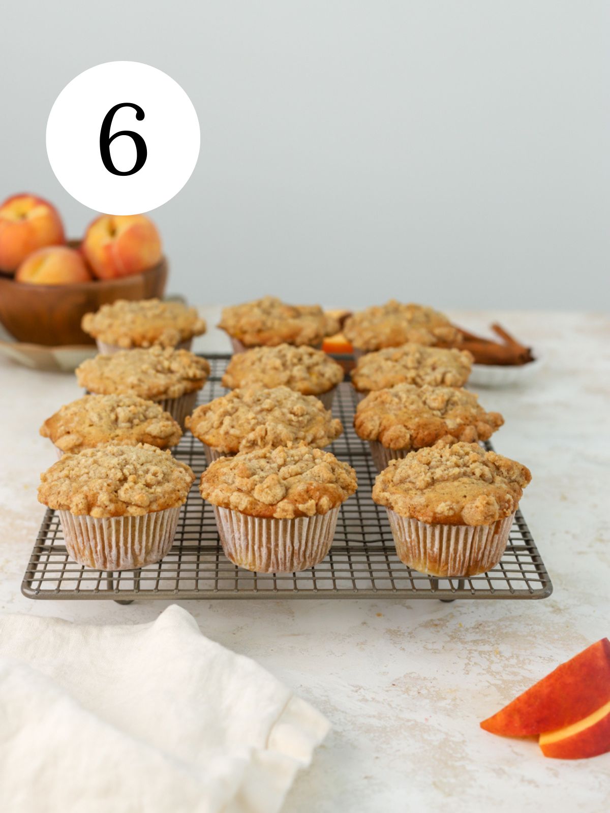 Peach cobbler muffins on a rack next to a bowl of peaches. 
