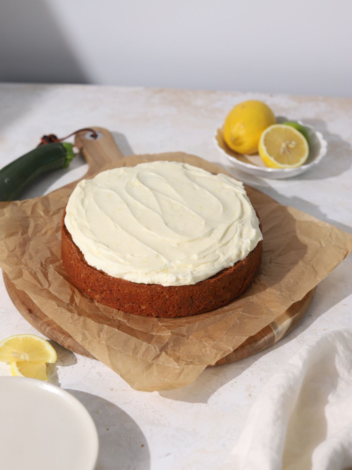 A single layer round cake with frosting next to some lemons and a zucchini.