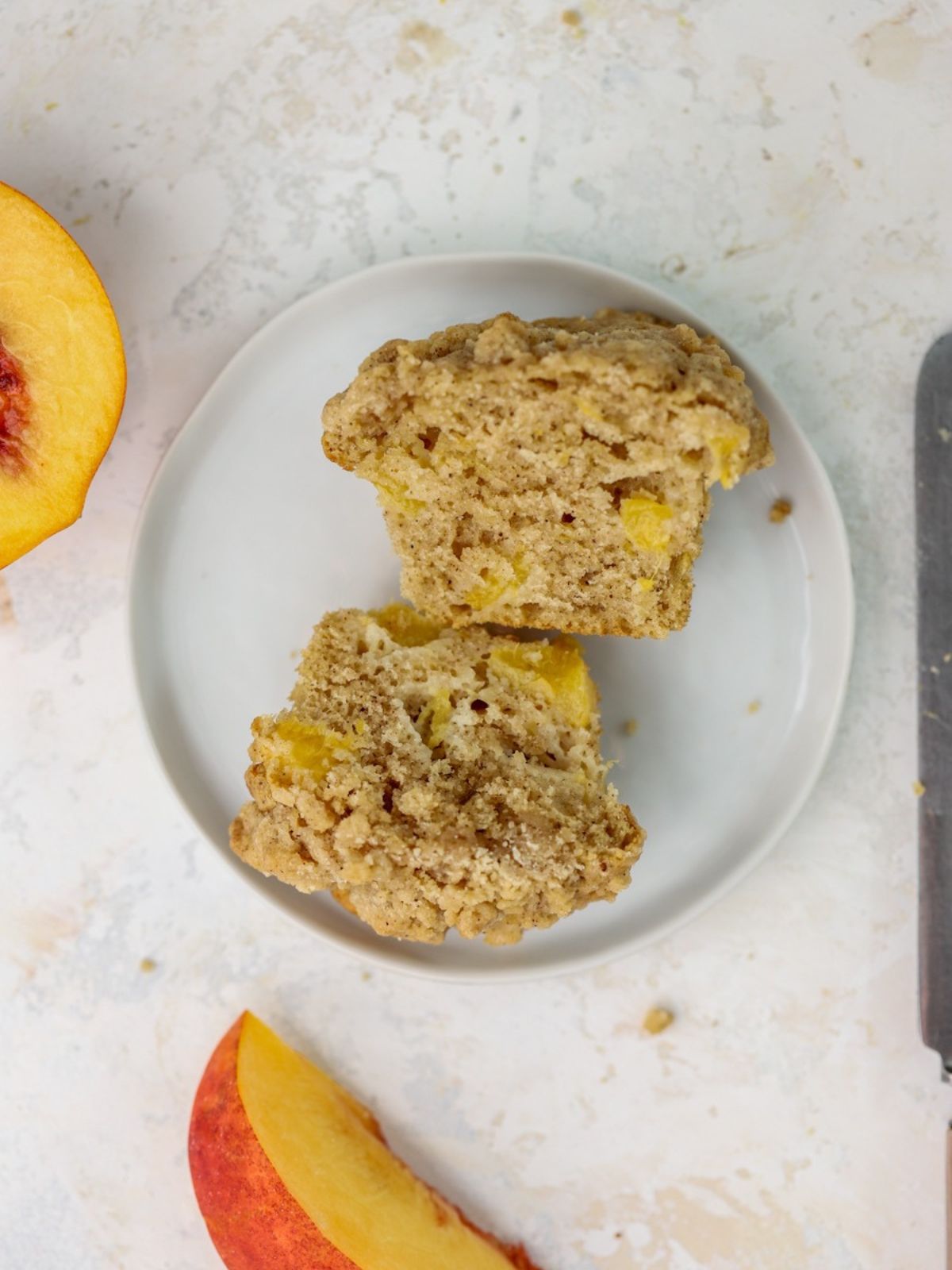 A peach muffin cut in half on a small white plate. 