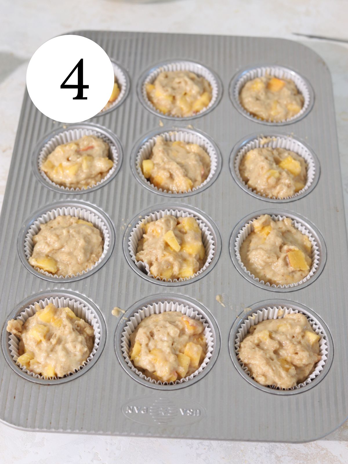 A muffin pan with paper liners filled with peach muffin batter. 
