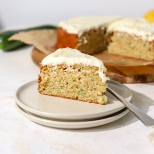 A slice of zucchini cake with frosting on a plate with a fork.