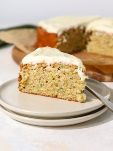A slice of zucchini cake with frosting on a plate with a fork.
