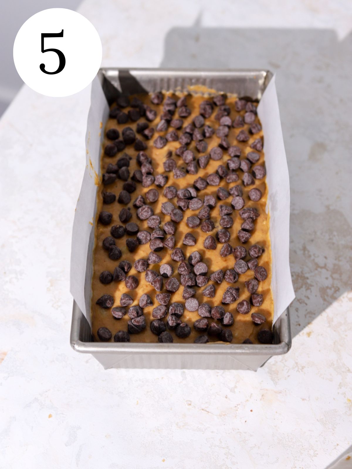 A loaf pan with pumpkin banana bread batter topped with chocolate chips.