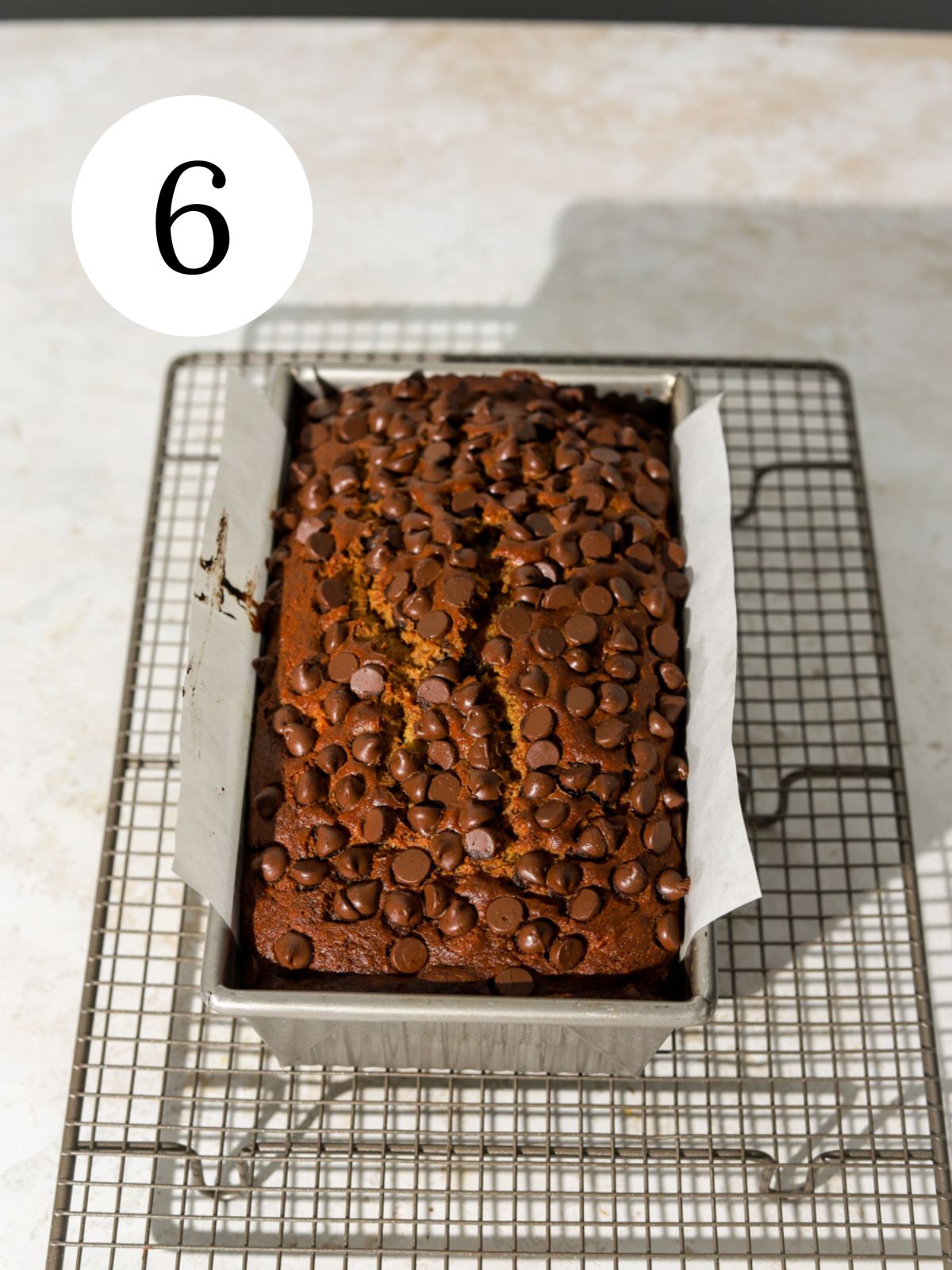 A loaf topped with chocolate chips in a pan on a wire rack.