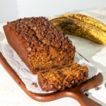 A loaf of banana pumpkin bread with chocolate chips on parchment paper.