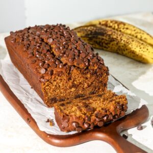 A loaf of banana pumpkin bread with chocolate chips on parchment paper.