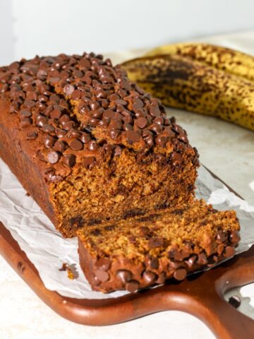 A loaf of banana pumpkin bread with chocolate chips on parchment paper.