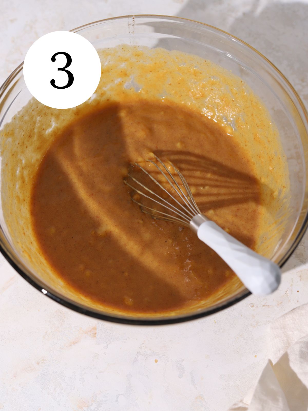 A glass bowl with pumpkin bread batter mixed with a whisk.