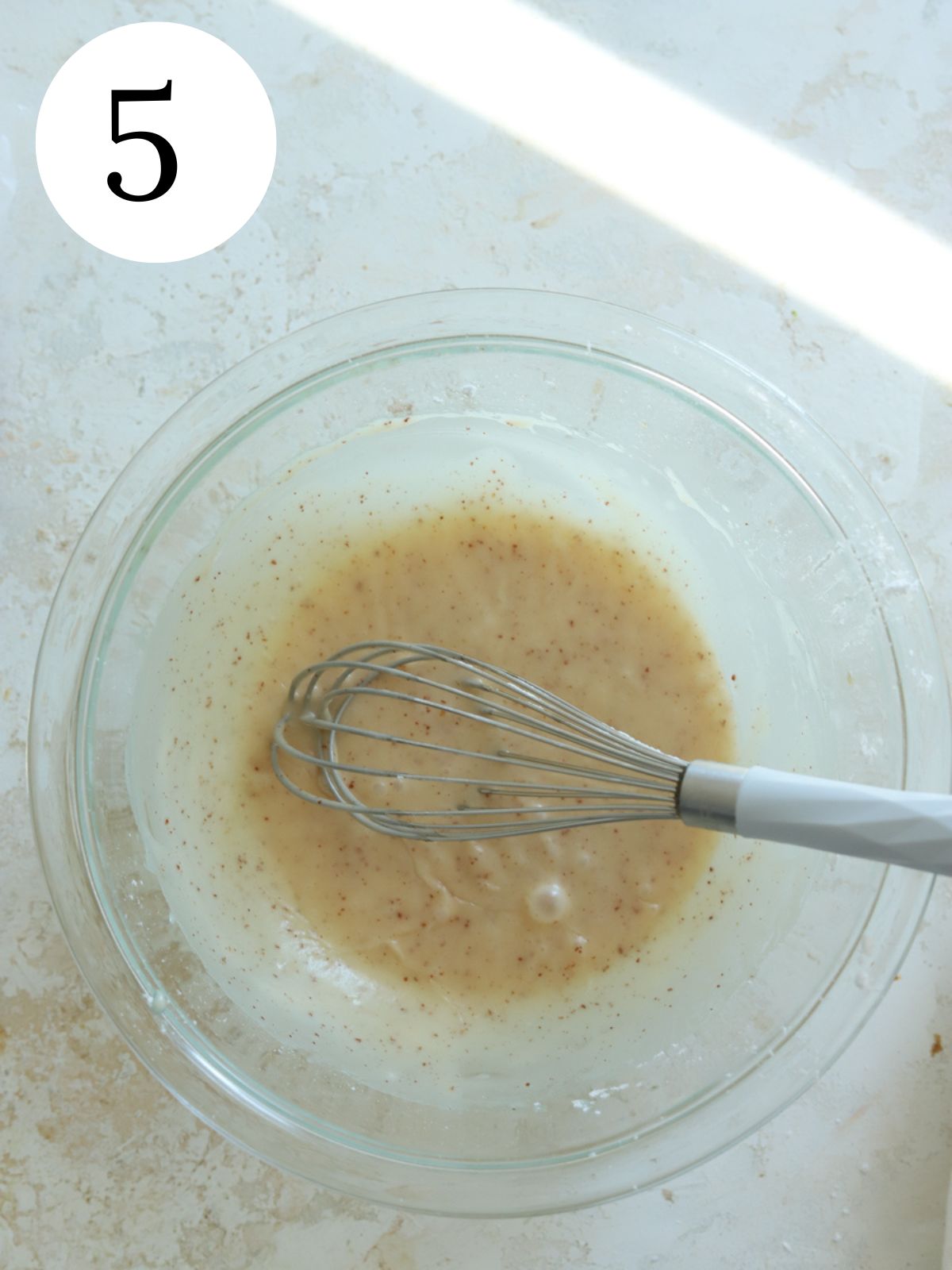 Brown butter glaze in a glass bowl with a whisk.