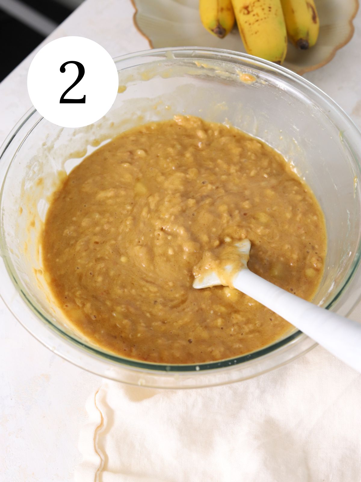 Banana cake batter in a glass bowl with a spatula. 