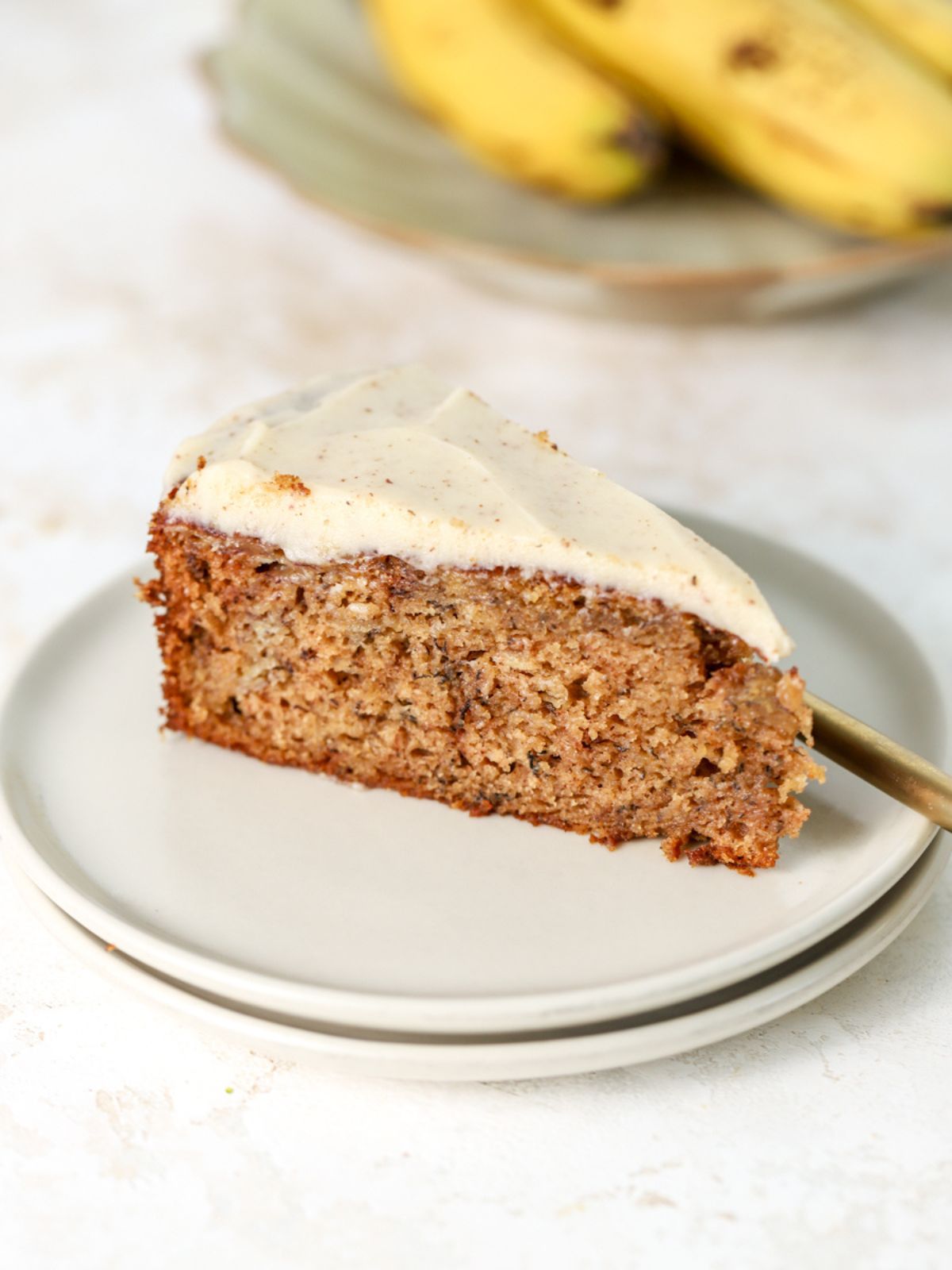 A slice of banana cake on a stack of two plates next to some bananas.