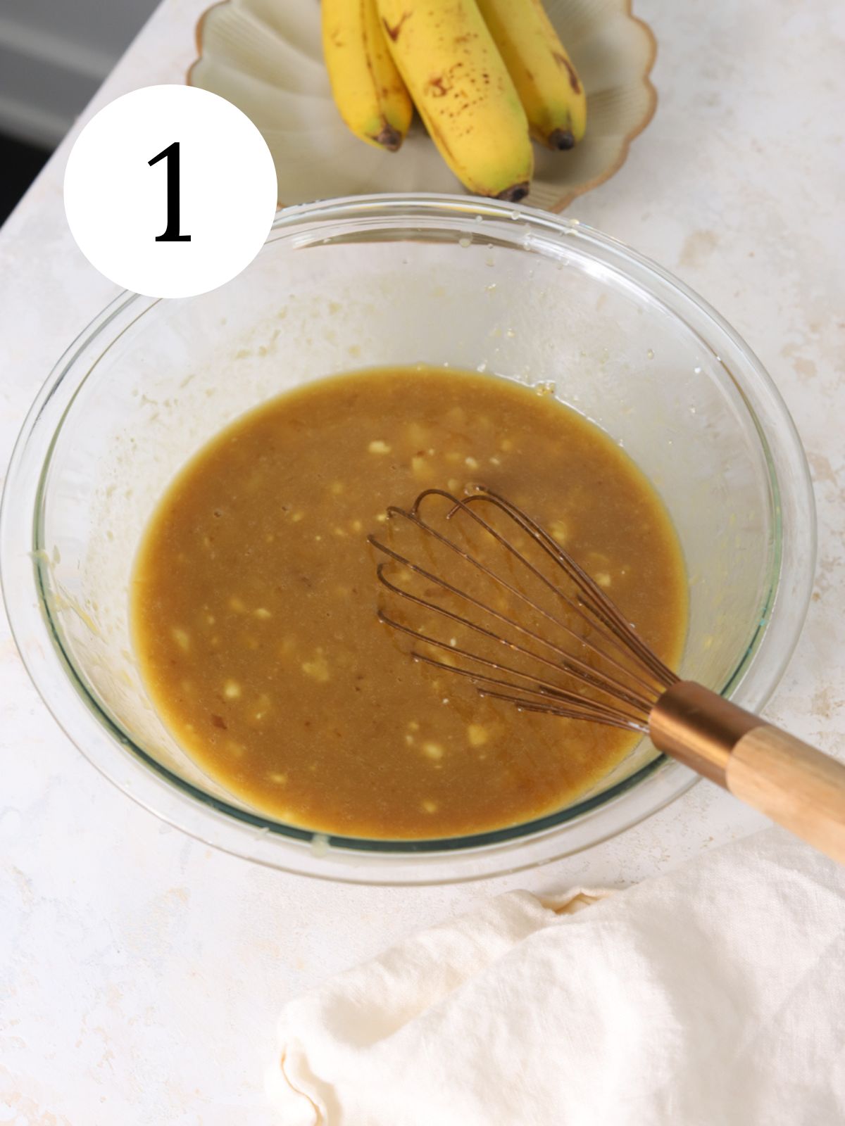 A glass mixing bowl with wet ingredients being whisked together.