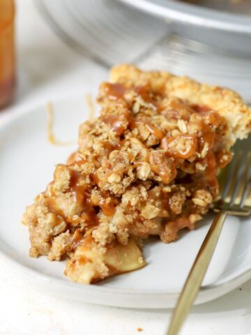 A slice of apple crumble pie topped with caramel sauce.