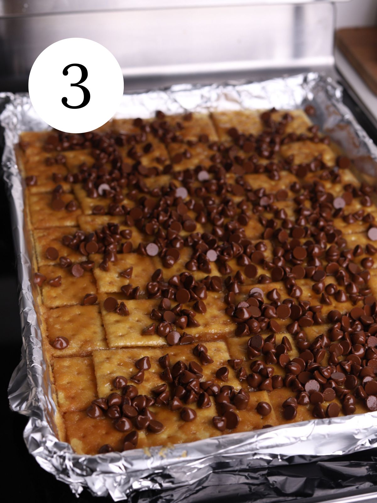 Saltines topped with toffee and chocolate chips on a baking sheet.