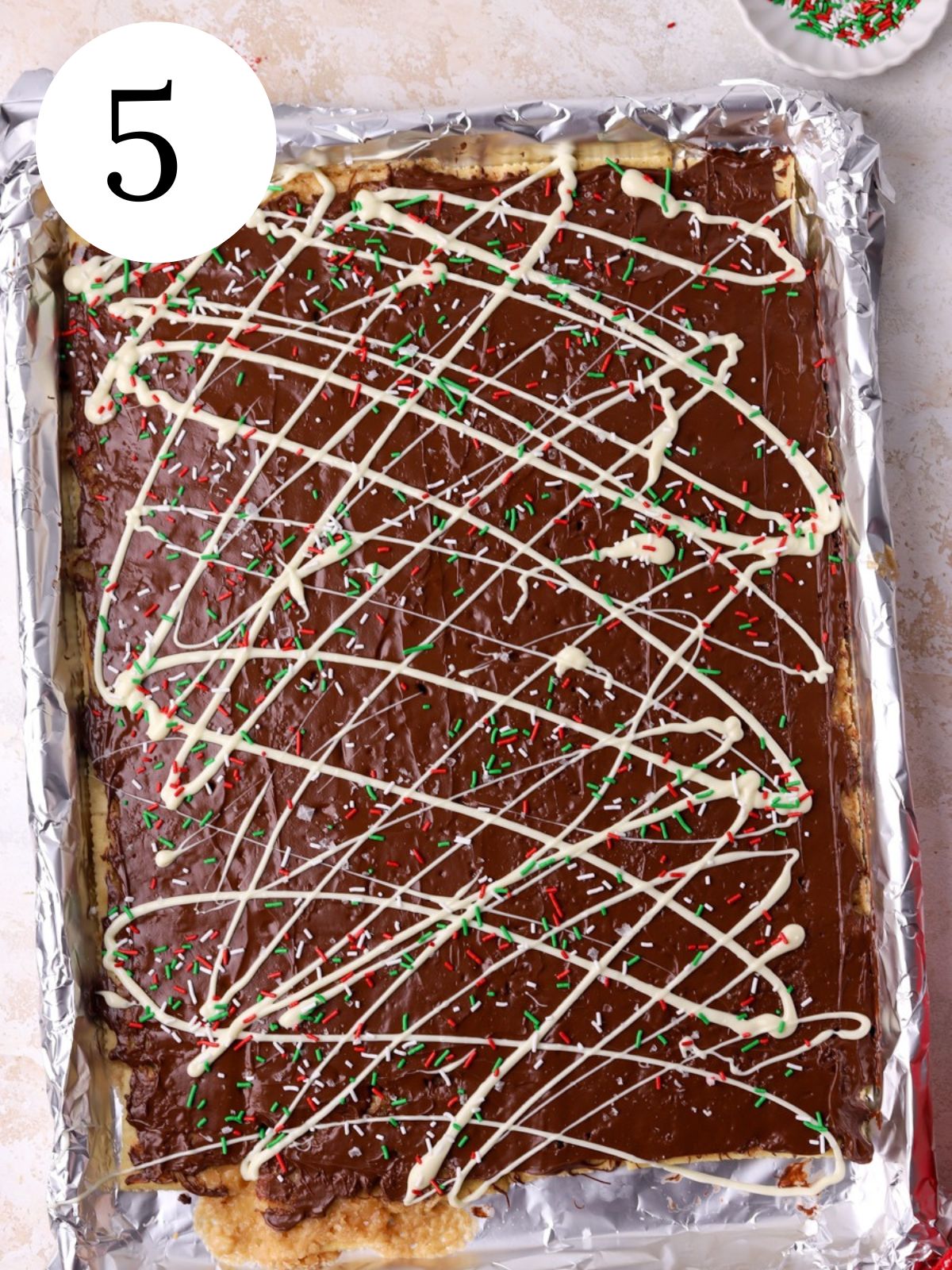 An aluminum foil lined baking sheet with christmas crack topped with sprinkles. 