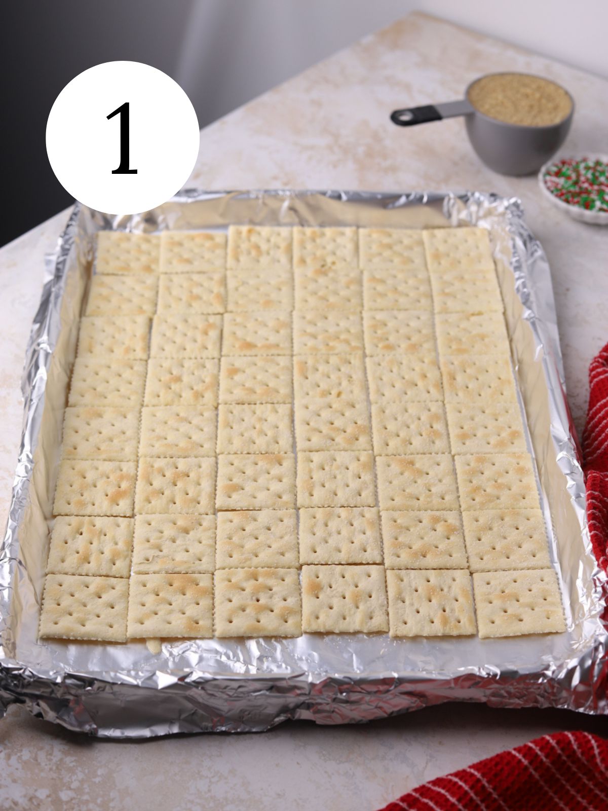 Saltine crackers spread in an even layer in a baking sheet lined with foil. 
