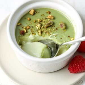 Pistachio panna cotta in a ramekin with a spoon in it.