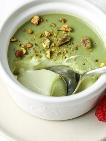 Pistachio panna cotta in a ramekin with a spoon in it.