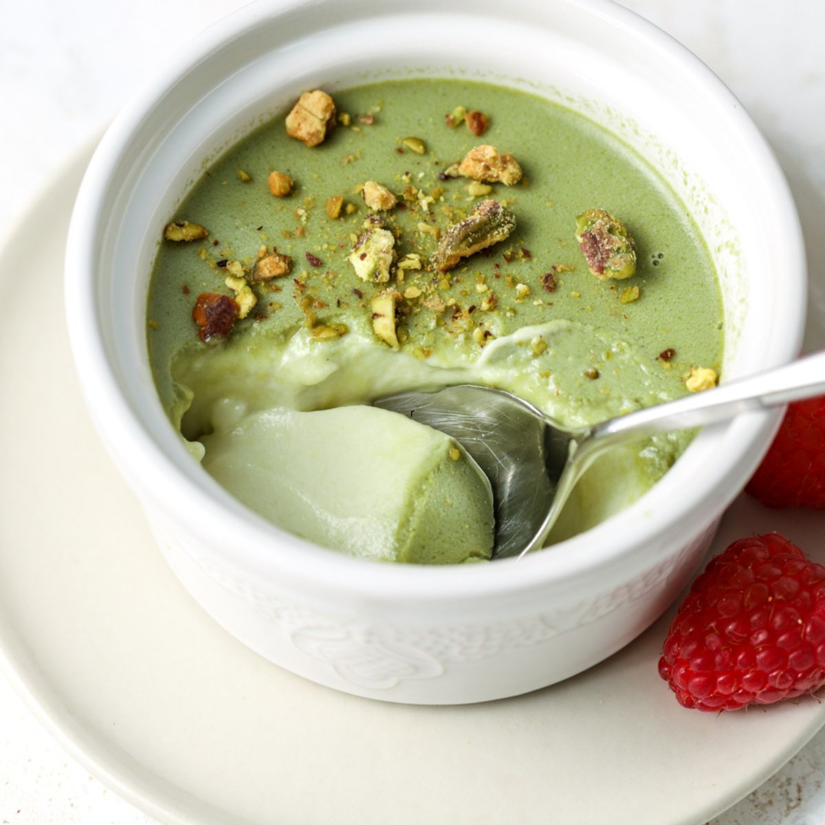 Pistachio panna cotta in a ramekin with a spoon in it.
