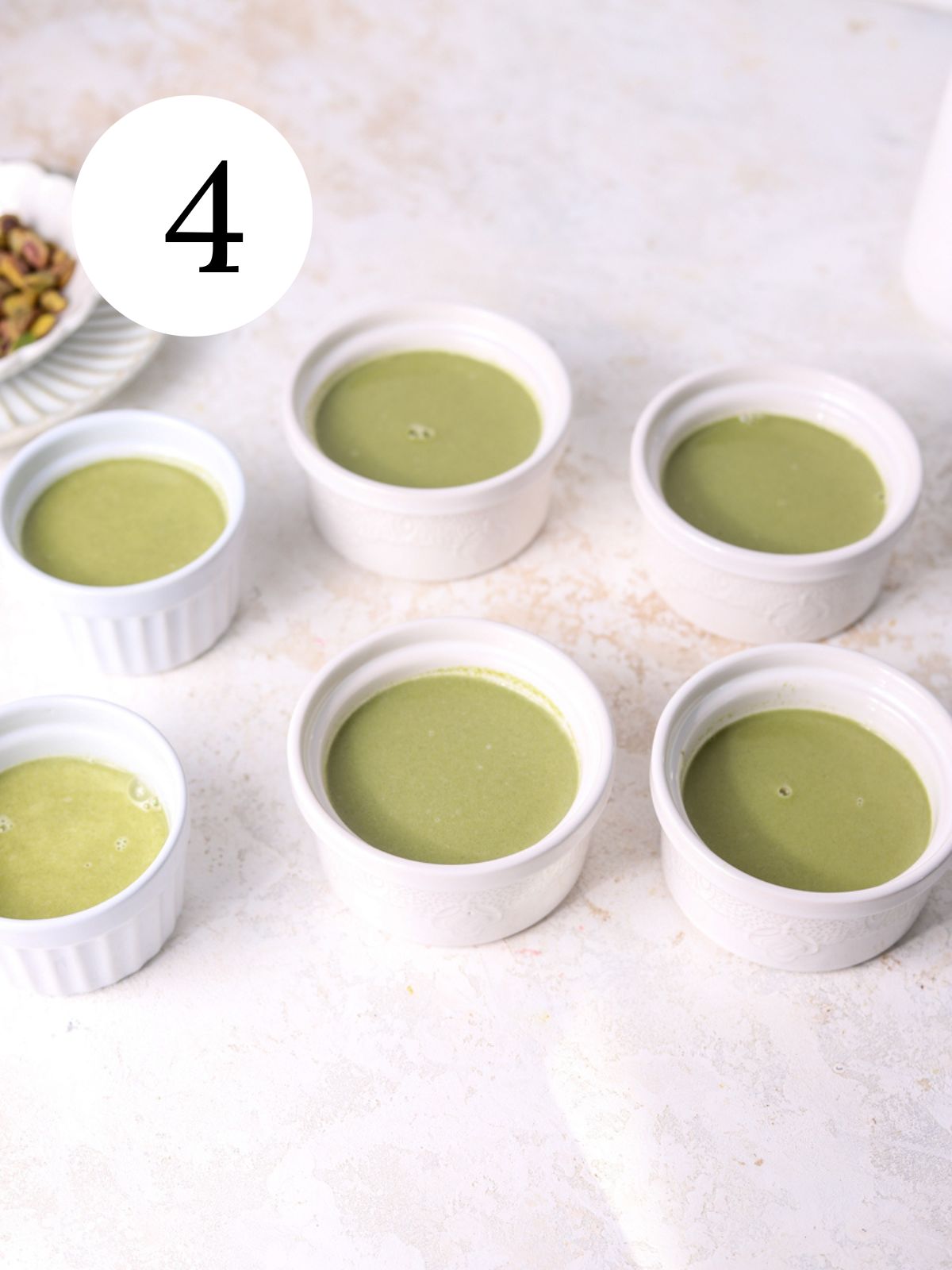 Ramekins filled with panna cotta and a bowl of pistachios.