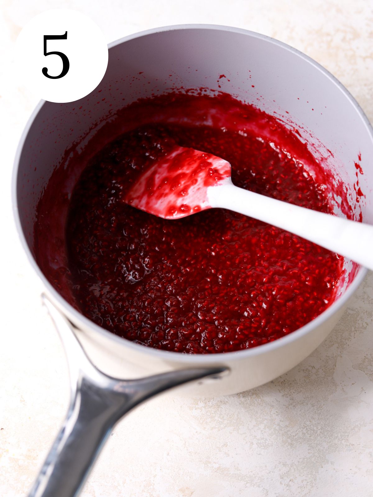A saucepan with raspberry compote and a spatula.