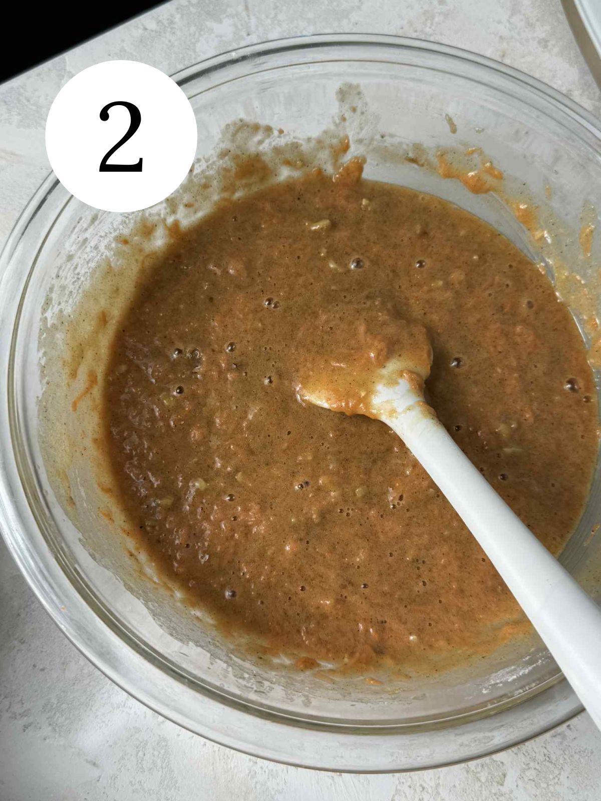 Carrot cake batter in a large glass bowl with a spatula.
