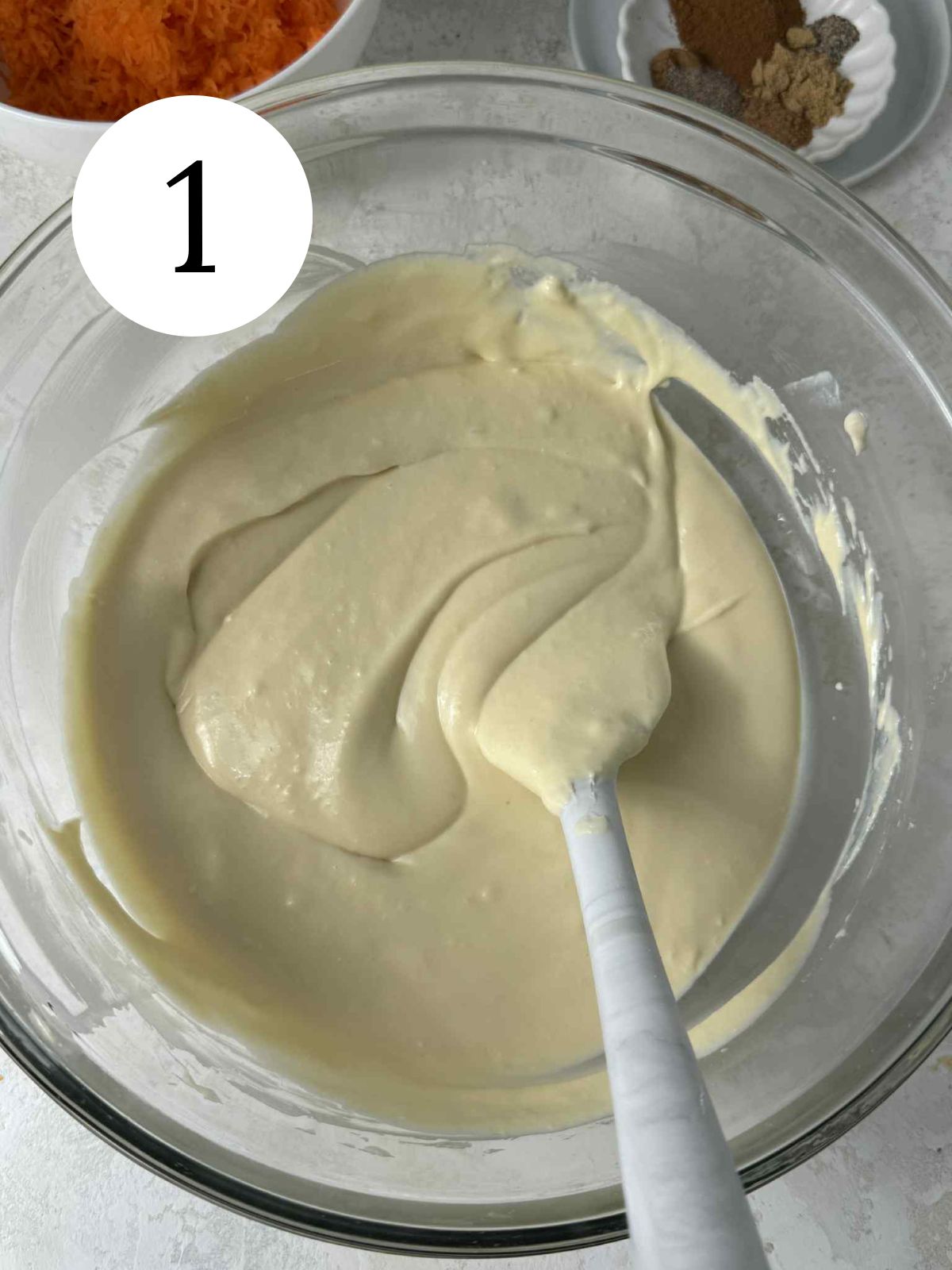 Cheesecake batter in a glass mixing bowl with a spatula.