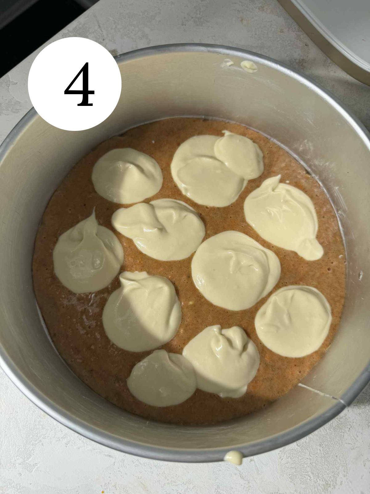Cheesecake dolloped over a layer of carrot cake in a pan.