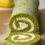A matcha cake roll with mascarpone filling being sliced.