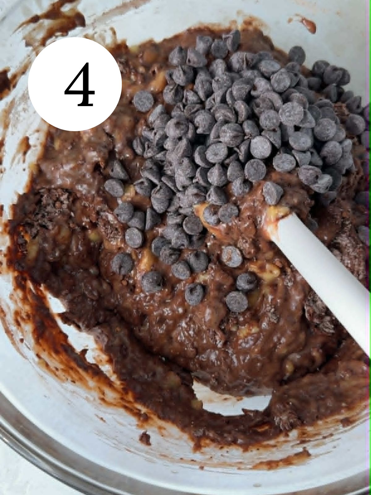 A spatula in a bowl with chocolate banana bread batter with chocolate chips.