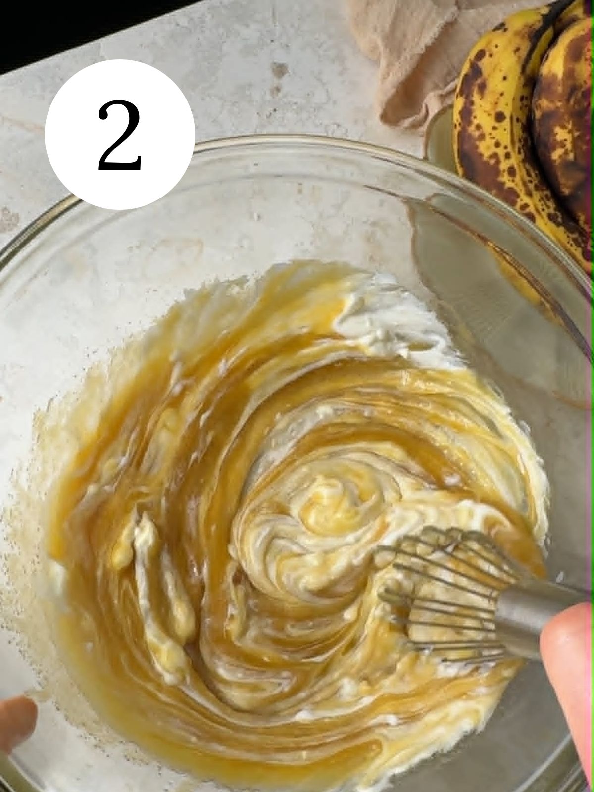 Whisking sour cream into batter in a bowl next to bananas.