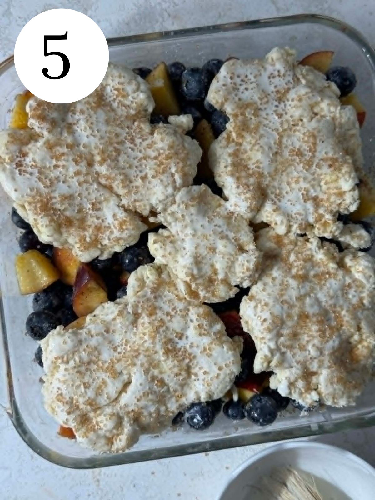 Cobbler topping spread over fruit, in a glass baking dish.